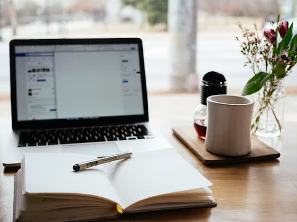 Laptop open to a short-form article beside a notebook and coffee